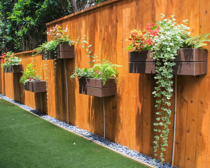 cour en gazon synthétique avec une haute clôture en bois montée avec des jardinières remplies de belles plantes à fleurs