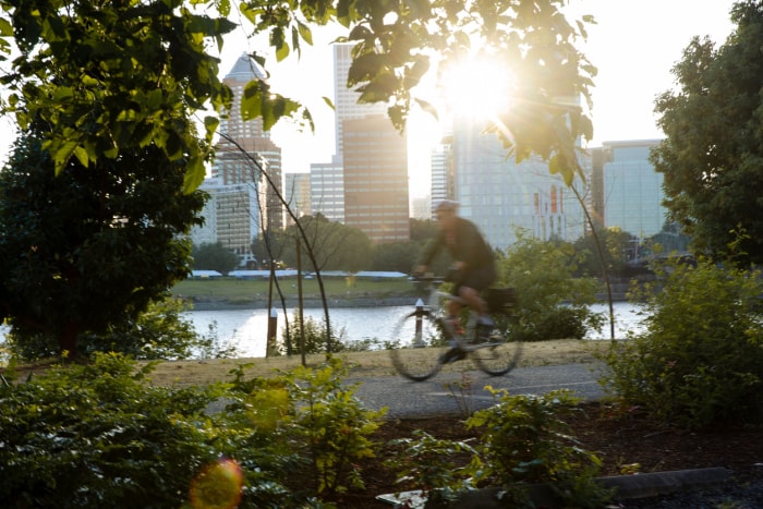 Un cycliste roule sur une piste cyclable le long de la rivière à Portland avec vue sur la ville de l'autre côté de l'eau.