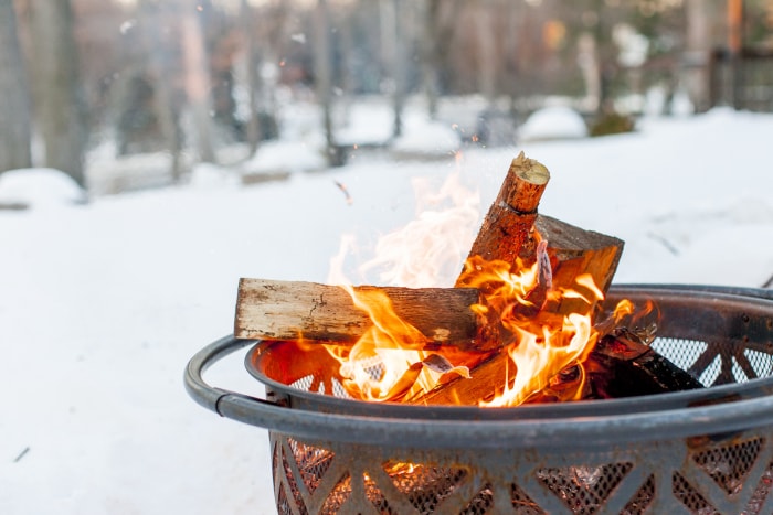 Gros plan d'un feu de joie pendant la saison hivernale. Le feu est à l'intérieur d'un foyer en métal. Scène enneigée et bois en arrière-plan.