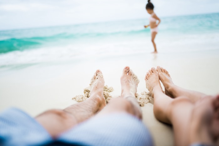 angle de vue de deux paires de jambes sur la plage avec une petite fille jouant sur le rivage