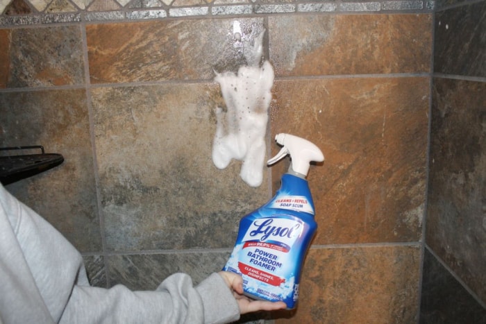 Une personne tenant un flacon pulvérisateur de Lysol Power Bathroom Foamer Cleaner après l'avoir pulvérisé sur le carrelage de la douche lors d'un test.