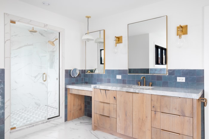 Grande salle de bains avec carrelage bleu et blanc, double meuble-lavabo en bois et accessoires en laiton.