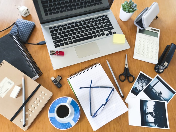 bureau en bois clair recouvert d'une tasse à café pour ordinateur portable, d'agendas, de photographies et d'autres fournitures de bureau