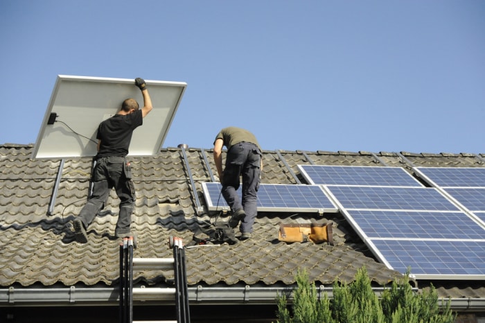 Deux ouvriers installent des panneaux solaires sur un toit en tuiles.