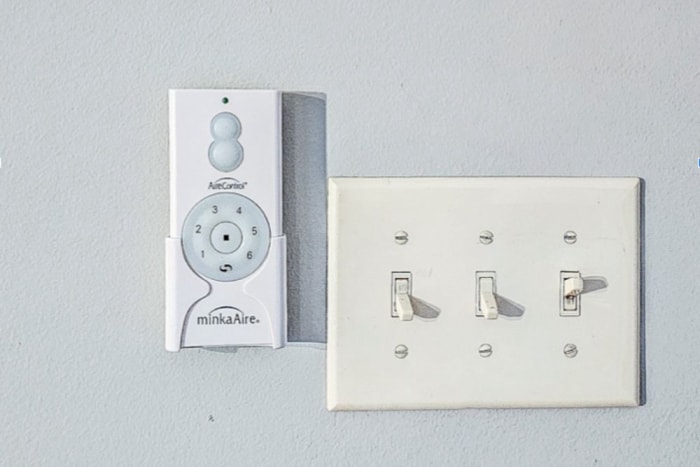 La télécommande du ventilateur de plafond Barn by Minka-Aire est installée sur le mur à côté d'un interrupteur.