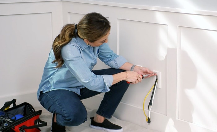 Femme cachant des fils à l'intérieur d'un mur blanc à l'aide d'un conduit en PVC.