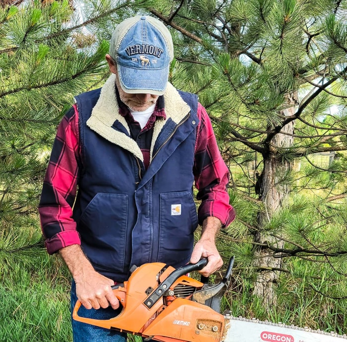 Un homme portant la veste Carhartt Flame-Resistant Sherpa-Lined Vest et tenant une tronçonneuse.