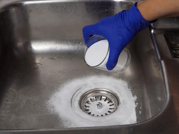 Main gantée versant du bicarbonate de soude à partir d'un verre dans le drain de la cuisine.