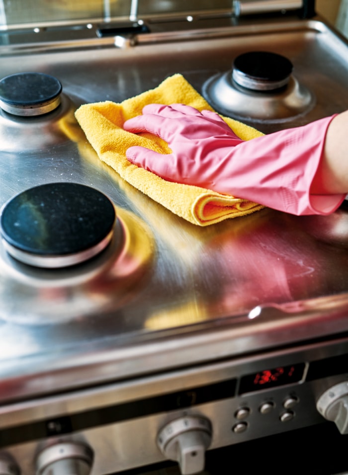 une main dans un gant rose essuie la plaque de cuisson en acier inoxydable avec un chiffon en microfibre jaune