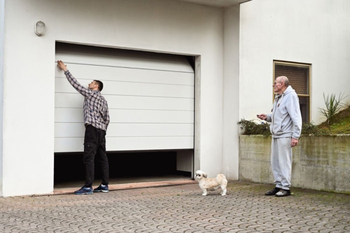 Deux hommes et un chien se tiennent devant une porte de garage.