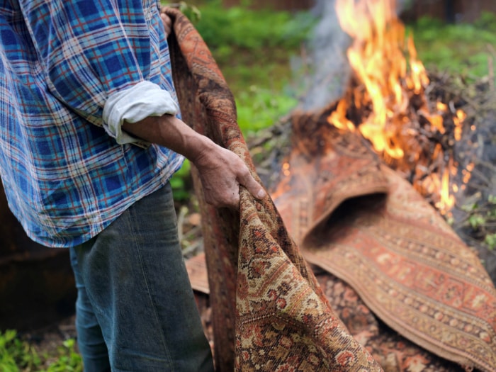 Une personne jette une tapisserie dans un tas de branches en feu.