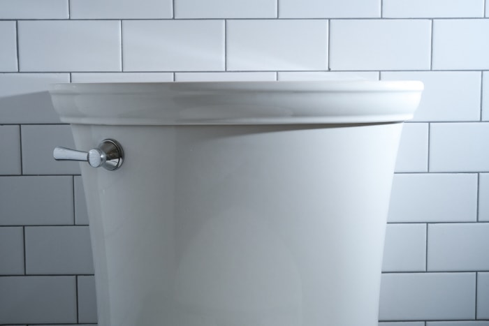 Un réservoir de toilette blanc d'apparence coûteuse avec un couvercle décoratif et un clapet en nickel brossé.