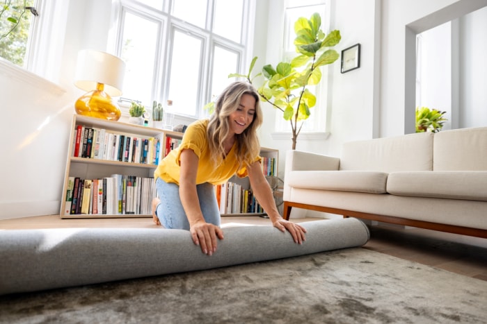 Femme déroulant un épais tapis dans le salon.