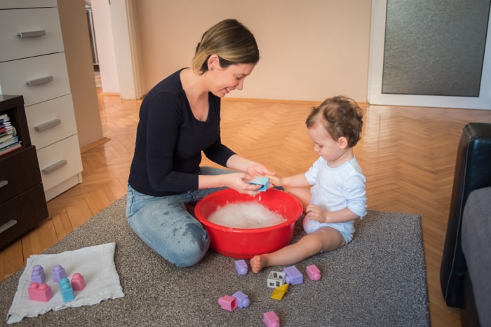 Jeune mère, femme, lavant des jouets avec son fils en bas âge dans un salon. Un enfant en bas âge s'amuse avec des jouets et de l'eau, fait des bulles, et profite de son temps de complicité avec sa mère. Coronavirus, covid 19 quarantaine.