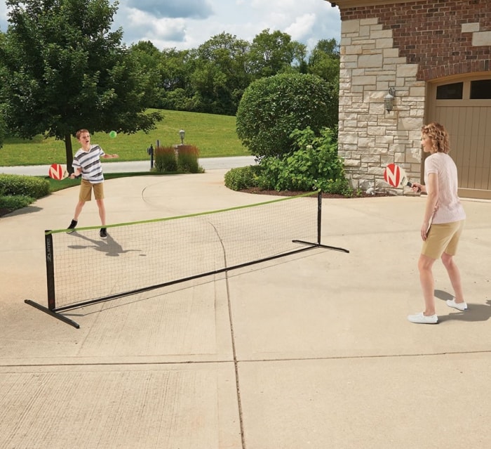 Deux personnes jouent au pickleball sur un filet dans leur allée.