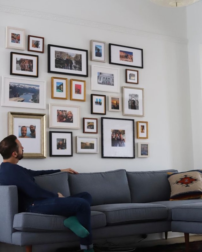 Homme assis sur un canapé regardant le mur d'une galerie de photos.