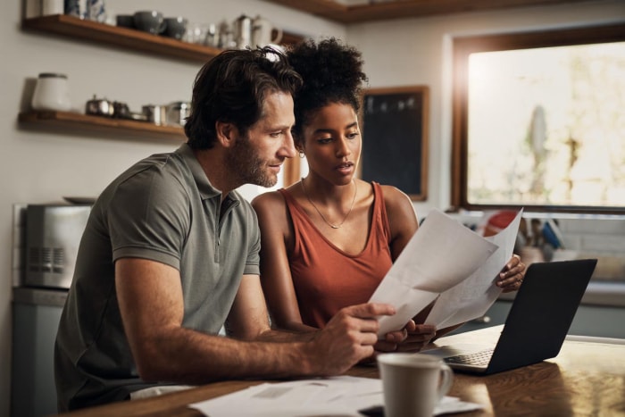 Un homme et une femme consultent des documents devant un ordinateur portable.