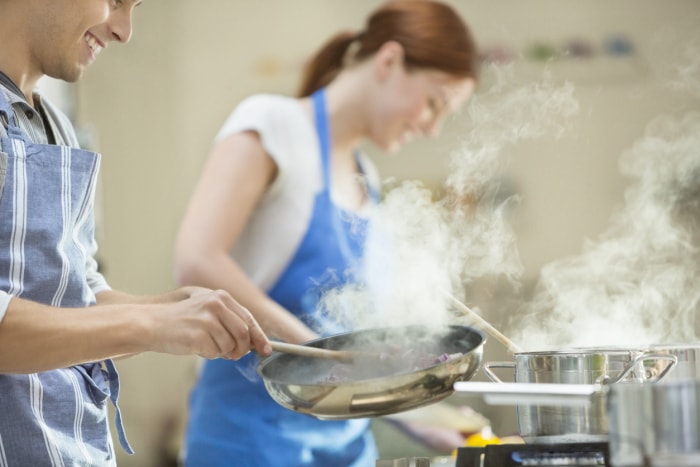 Couple cuisinant dans une cuisine avec de la fumée s'élevant des poêles et des casseroles