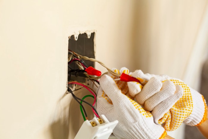 Système électrique dans un mur en cours de réparation par une personne portant des gants.