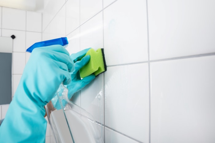 Mains gantées utilisant un nettoyant en spray et une éponge sur le coulis de la salle de bain.