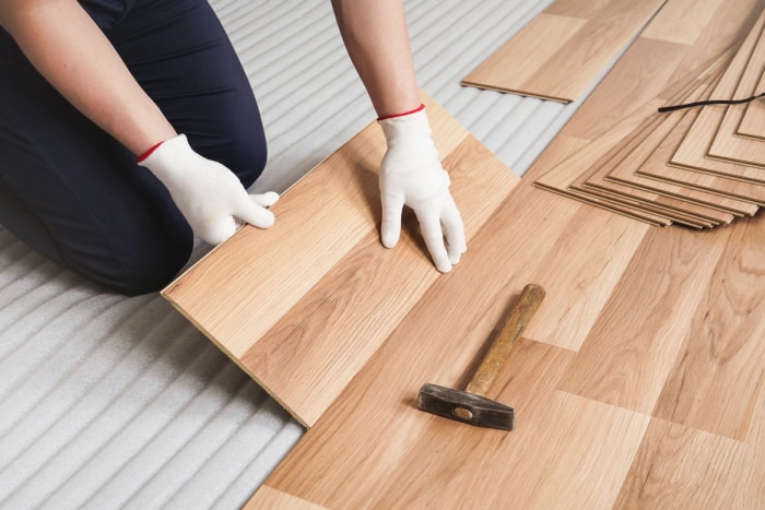 Une personne portant des gants blancs installe un parquet stratifié en bois.