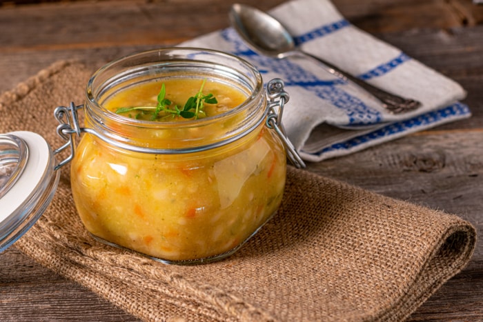 Soupe ou ragoût frais et fait maison dans un bocal, servi isolé sur une table rustique en bois. Vue rapprochée