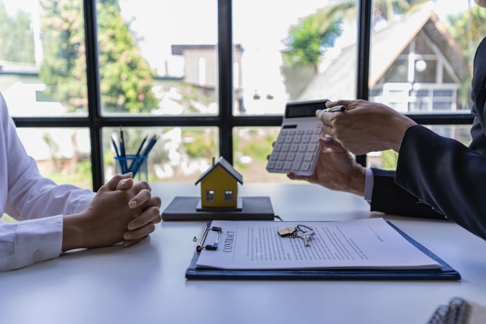 un homme tenant une calculatrice pour montrer à quelqu'un d'autre une maison sur la table illustrant un concept immobilier