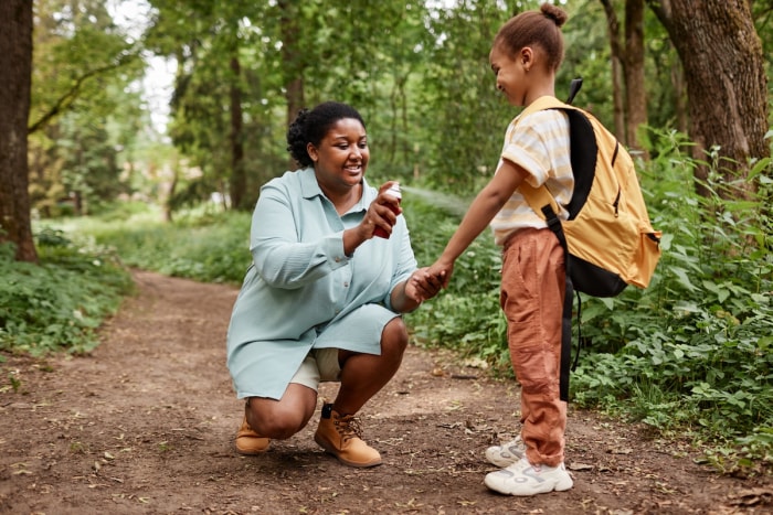 Une mère sur un sentier de randonnée pulvérise un produit anti-moustique sur son enfant.