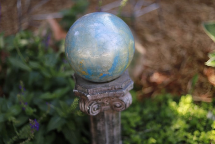 Une boule de jardin argentée-métallique est posée sur un pilier dans un jardin.