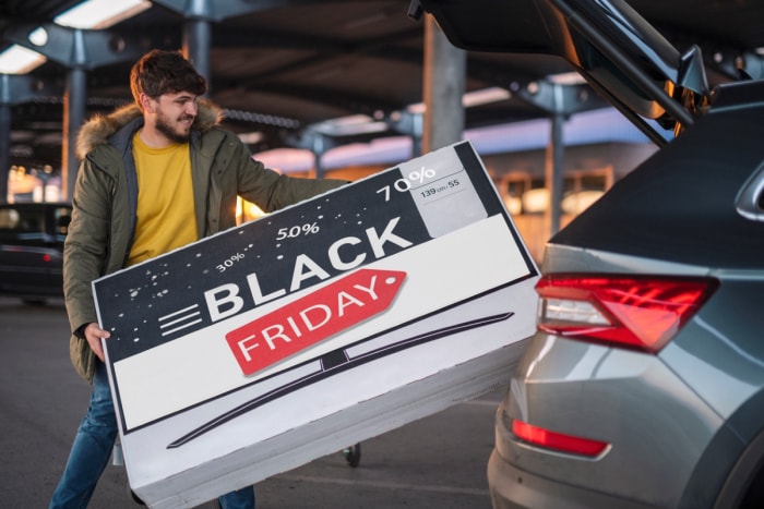 Un homme met une boîte Black Friday dans une voiture.