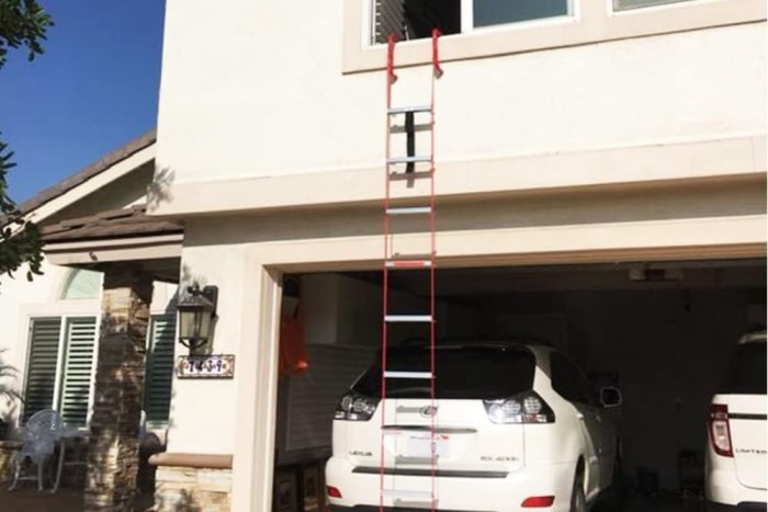 Une maison avec la porte du garage ouverte et une voiture à l'intérieur avec une échelle de secours suspendue à une fenêtre ouverte.