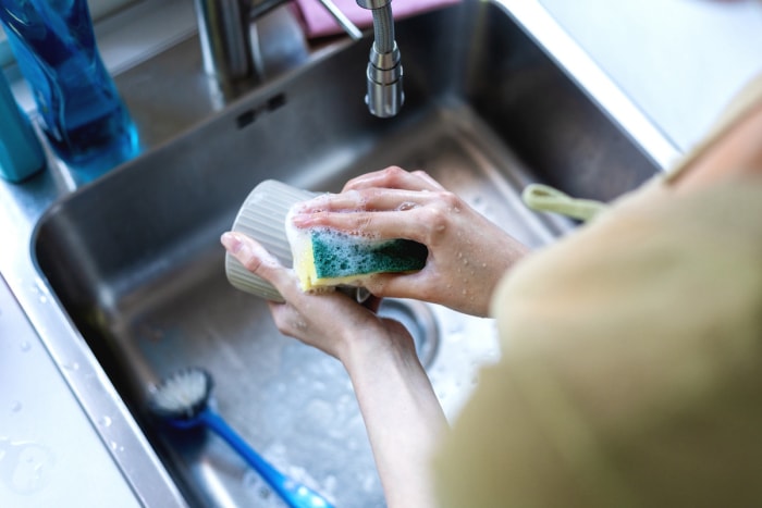 Une femme lave une tasse blanche dans un évier de cuisine avec une éponge à récurer.