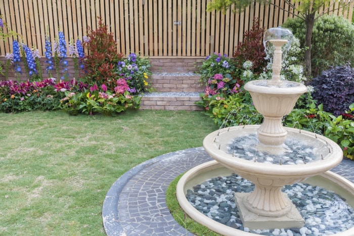 Un jardin clôturé avec des fleurs colorées et une fontaine à plusieurs niveaux.