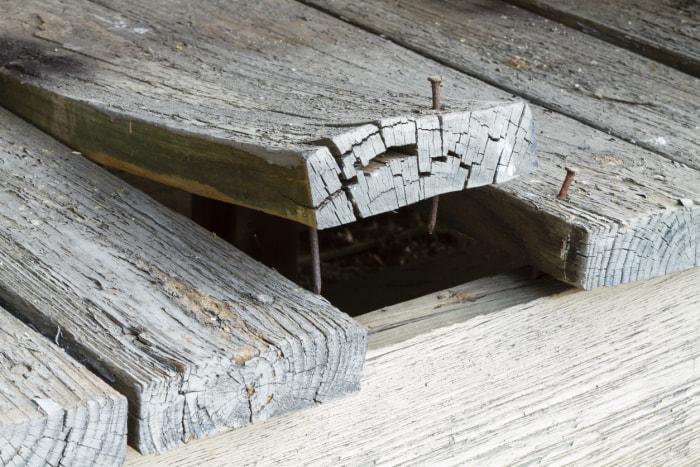 Un ensemble de vieilles planches de terrasse extérieures fissurées et écaillées sur une maison, dont l'une s'est beaucoup déformée et s'enroule à cause de l'exposition aux éléments extérieurs.