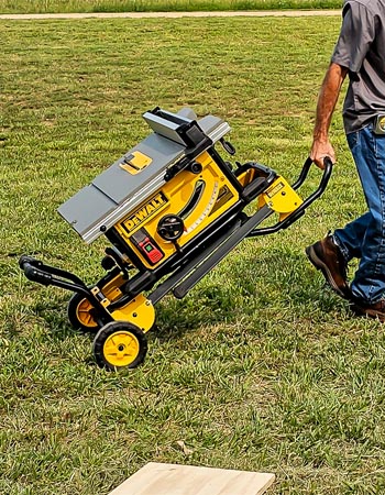 Une personne tirant la scie à table DeWalt de 10 pouces dans une cour à l'aide de son support roulant