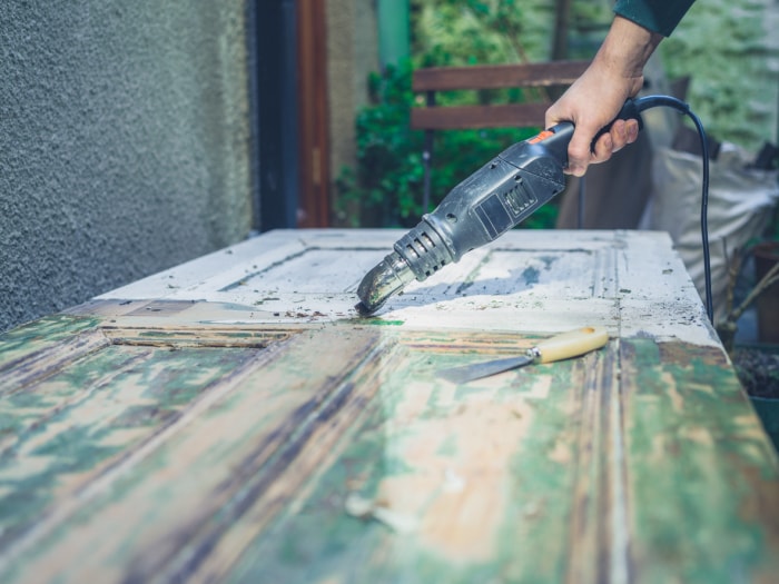 La main d'un jeune homme enlevant la peinture d'une porte avec un pistolet thermique