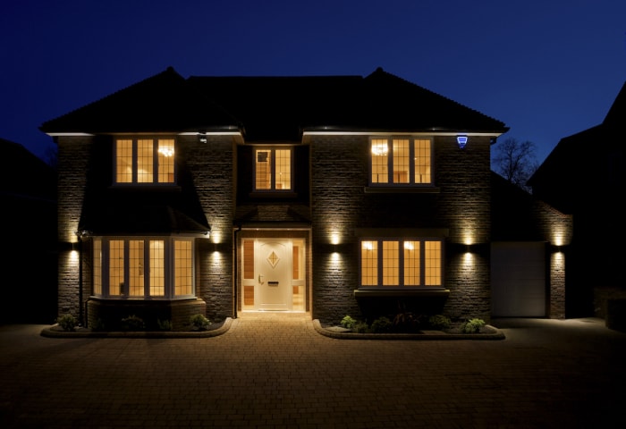 La façade et l'allée d'une maison de luxe, prises au crépuscule avec toutes les lumières intérieures et extérieures allumées. 