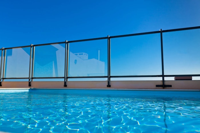 Une clôture en verre entoure une piscine creusée.