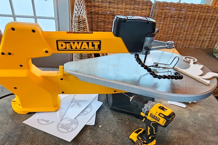 La scie à chantourner à vitesse variable DeWalt de 20 pouces est installée sur un établi avec une perceuse et plusieurs modèles.