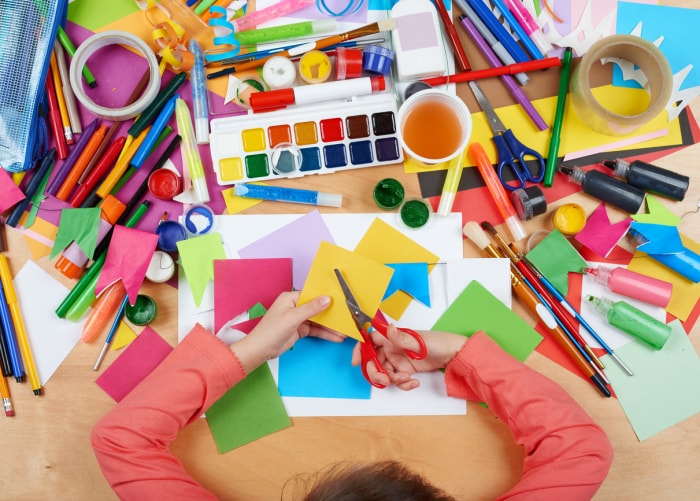 Vue aérienne d'un enfant faisant du bricolage à une table recouverte de papier, de peinture et d'autres fournitures.