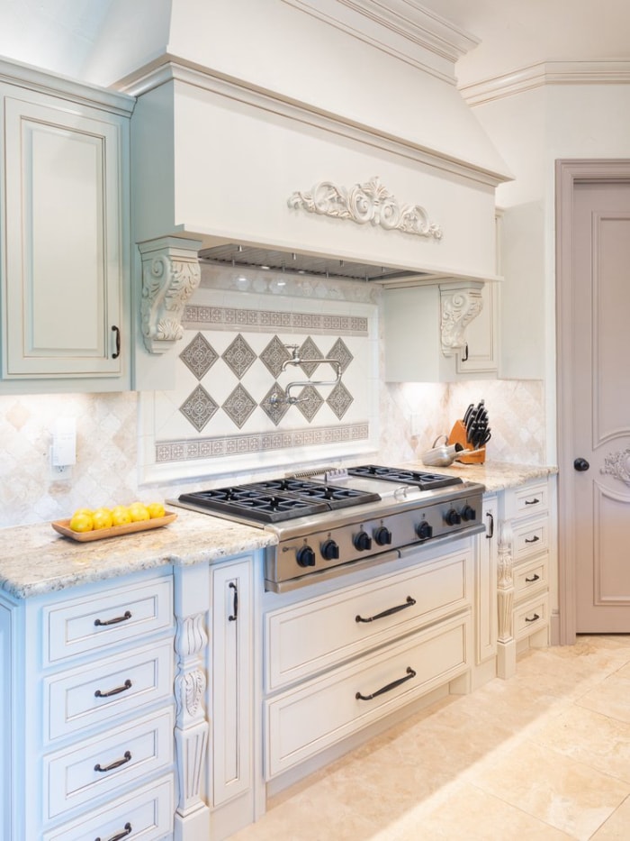 Panneau de dosseret argenté et blanc personnalisé et décoré installé derrière une cuisinière à gaz dans une cuisine blanche