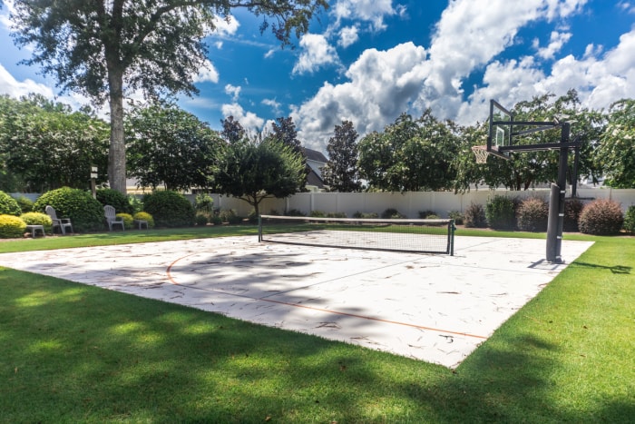 Une grande cour arrière avec de l'herbe verte et un terrain de basket-ball qui a été transformé en terrain de pickleball à domicile.