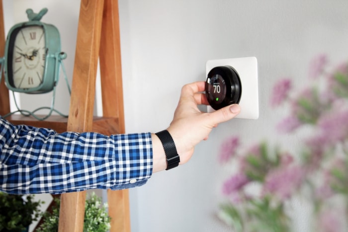 Homme réglant la température sur un thermostat intelligent fixé au mur.