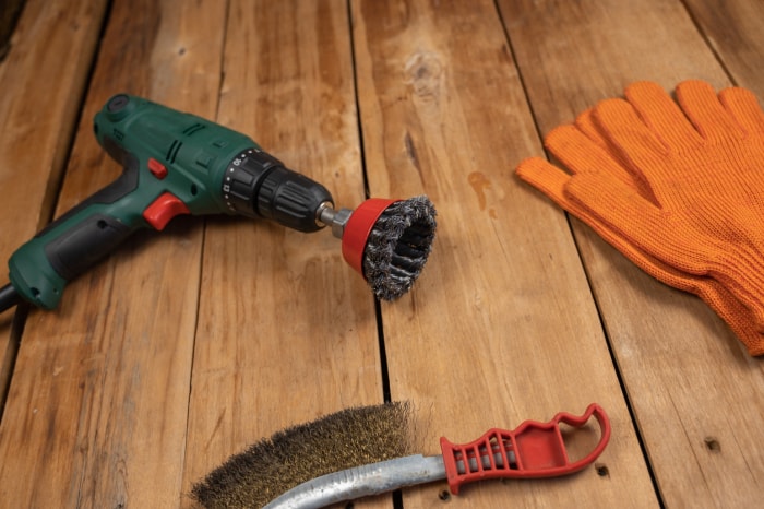 Perceuse électrique, brosse métallique, brosse métallique et gants orange. Outils manuels et électriques posés sur les planches. Travail du bois. Vue de dessus. Mise au point sélective.