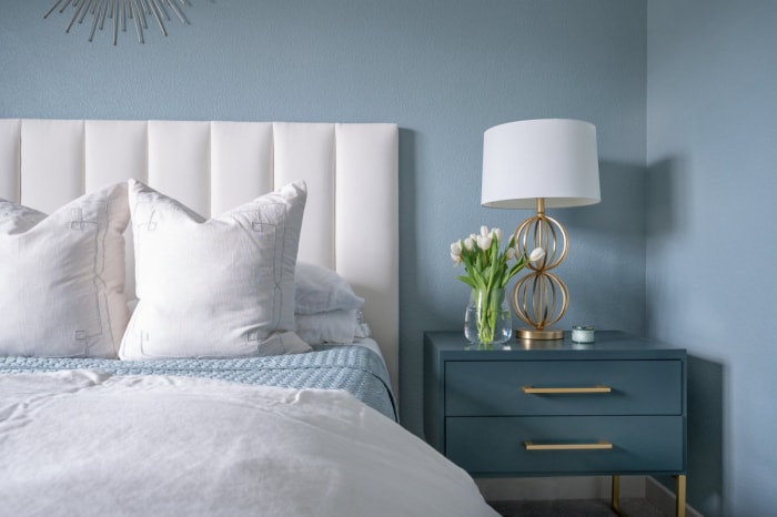 Un lit blanc et une table de nuit bleue sont placés contre un mur peint en bleu.