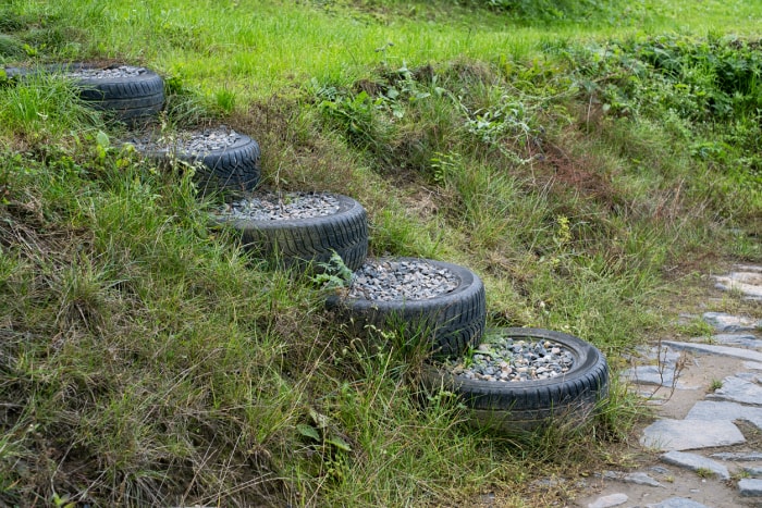 Vieux pneus de voiture d'occasion remplis de pierres de granit pour faire des escaliers sur la pente du jardin.