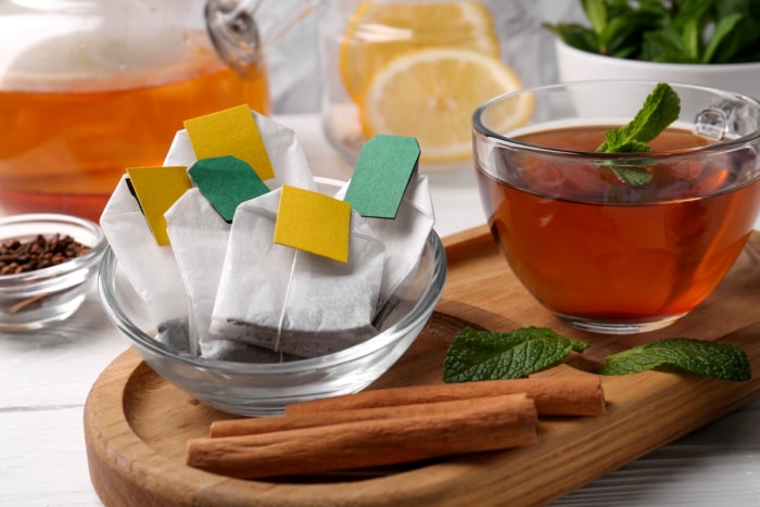 Sachets de thé dans un bol transparent à côté d'une tasse de thé.