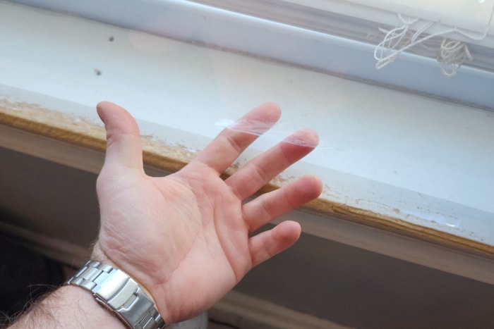 Une personne passant ses doigts sous une couche du meilleur kit d’isolation de fenêtre installé sur une fenêtre.