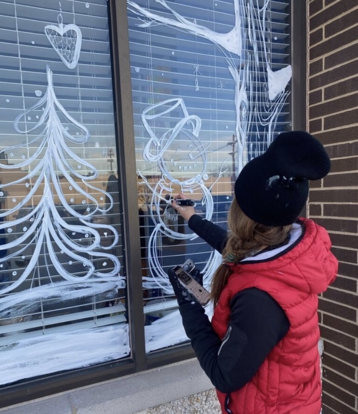 Une personne utilise de la peinture blanche pour esquisser un motif mural sur une fenêtre.