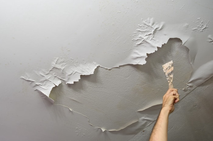 La main d'un homme arrache des bulles de peinture du plafond. 